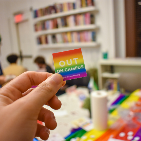 A hand holding a rainbow sticker that says 